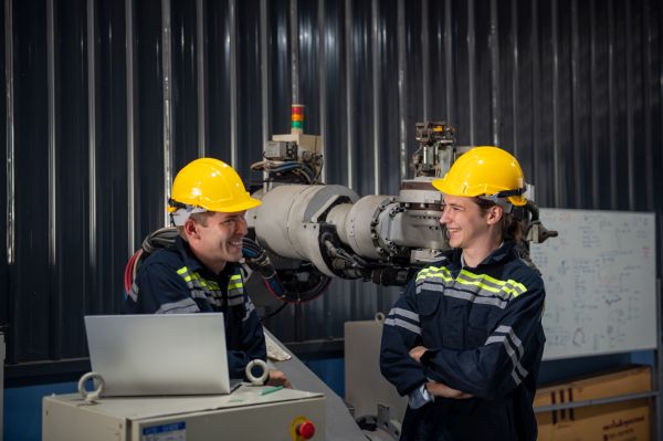 Ingenieur verhindert Maschinenstillstand durch den Austausch beim Schichtwechsel Ingenieur steht neben Roboterarm und bedient Maschine in einer Industriefabrik
