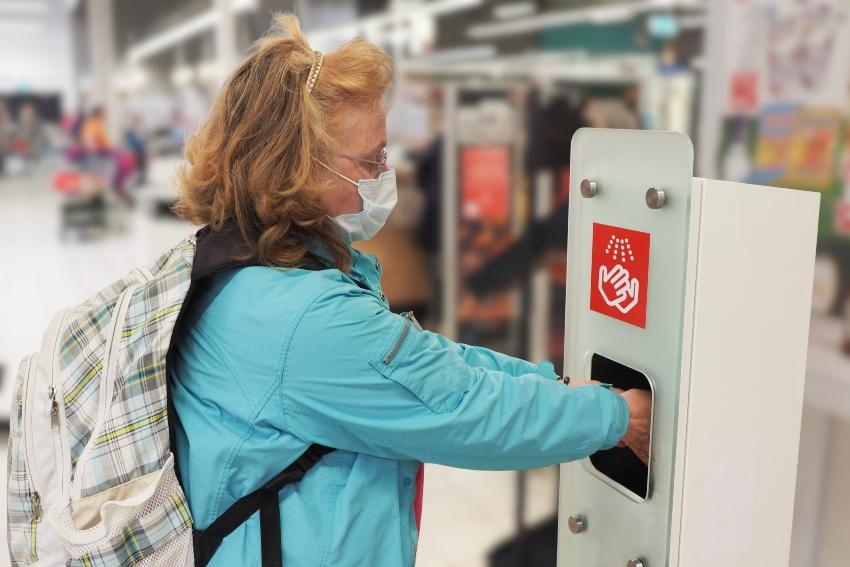 Frau nutzt Desinfektionsgerät in einem Supermarkt