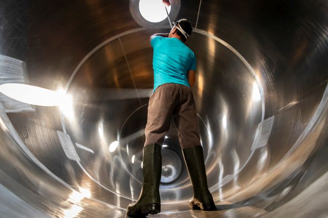 Mann steht in Gummistiefeln im Edelstahltank und reinigt die Öffnmung über seinem Kopf.