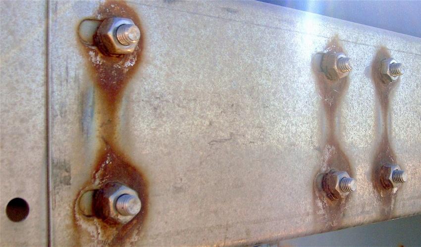 Schrauben und Muttern aus rostfreiem Stahl mit korrodierten Unterlegscheiben auf einer Grundplatte aus verzinktem Stahl - Korrosionsarten von Metall