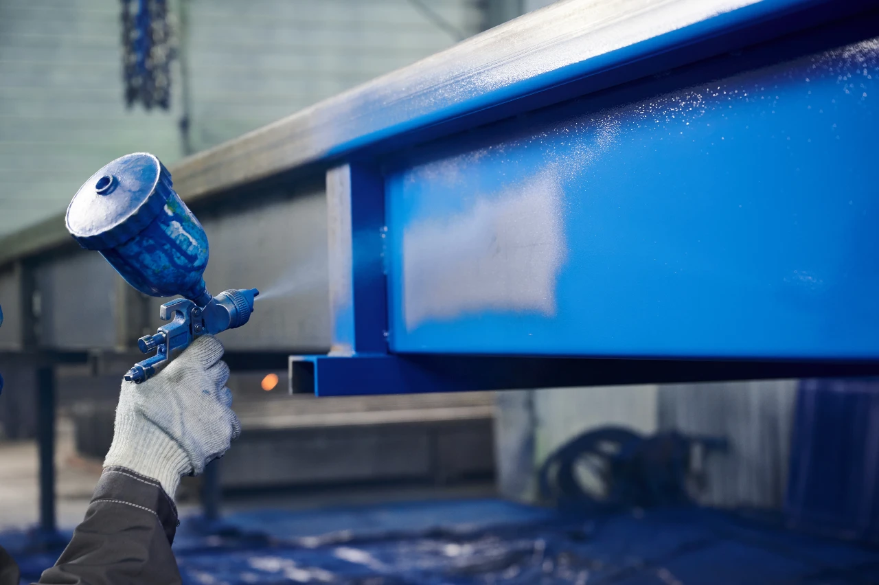 Arbeiter besprüht Stahlträger mit blauer Lackfarbe